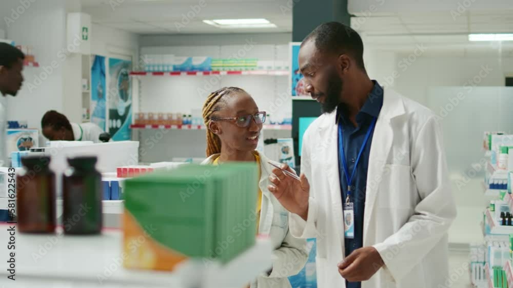 Man and woman looking at medicaments on shelves, trying to find prescription treatment and vitamins. Young medic explaining healthcare to customer, showing box of medicine in drugstore. Man and woman looking at medicaments on shelves, trying to find prescription treatment and vitamins. Young medic explaining healthcare to customer, showing box of medicine in drugstore.