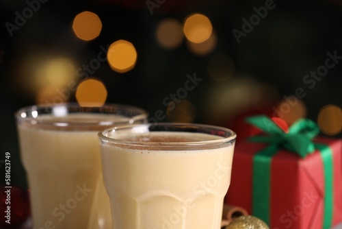 Tasty eggnog with cinnamon and gift box against blurred festive lights