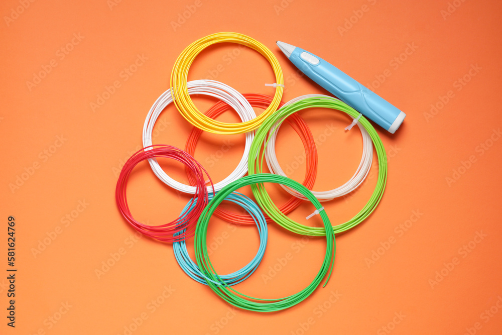 Fototapeta premium Stylish 3D pen and colorful plastic filaments on orange background, flat lay