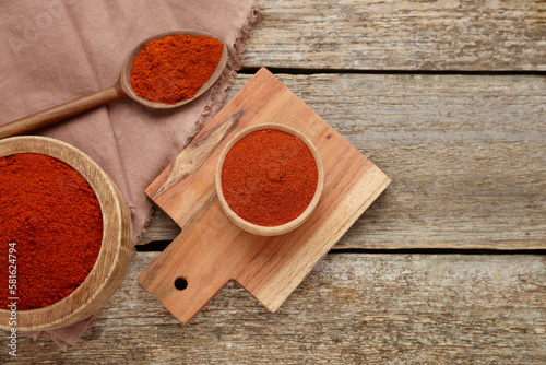 Fototapeta Naklejka Na Ścianę i Meble -  Bowls and spoon with aromatic paprika powder on old wooden table, flat lay. Space for text