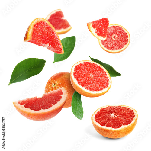 Cut fresh grapefruits and green leaves flying on white background