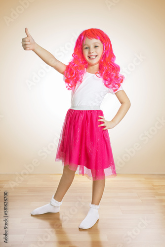 Beautiful little girl showing thumps up on beige background.