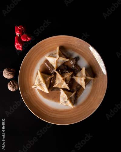 plato de pasta forma piramidal sobre plato dorado sobre fondo negro con nueces y pimientos photo