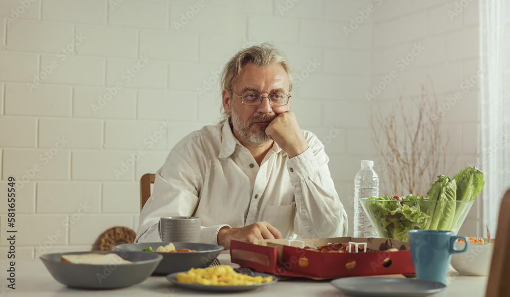 Elderly retired grandfather stay at home with unhappy face sitting alone on eating table in house. Depressed mature Senior old man upset feeling lonely and missing his family at home. Elderly retired grandfather stay at home with unhappy face sitting alone on eating table in house. Depressed mature Senior old man upset feeling lonely and missing his family at home.
