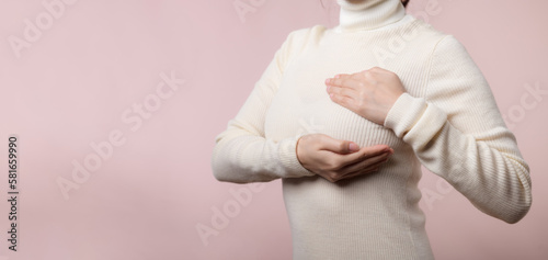 Woman hands checking lumps on her breast for signs of breast cancer on pink background. Healthcare world health day concept.