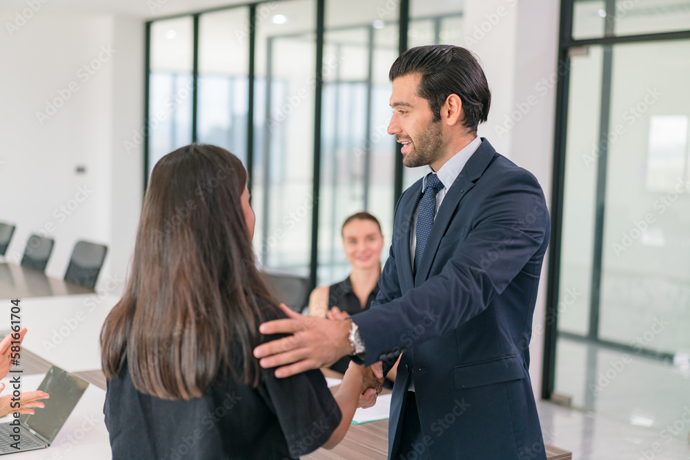 Friendly female manager shakes hands with her male colleague, congratulating him on job well done. Tam of business people applauding man during meeting in office. Business success concept.