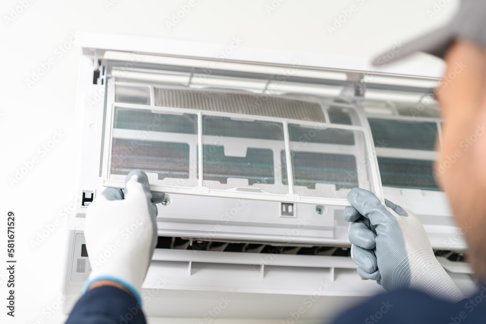 Air conditioner service indoors. Air conditioner cleaning technician He opened the front cover and took out the filters and washed it. He in uniform wearing rubber Air conditioner service indoors. Air conditioner cleaning technician He opened the front cover and took out the filters and washed it. He in uniform wearing rubber