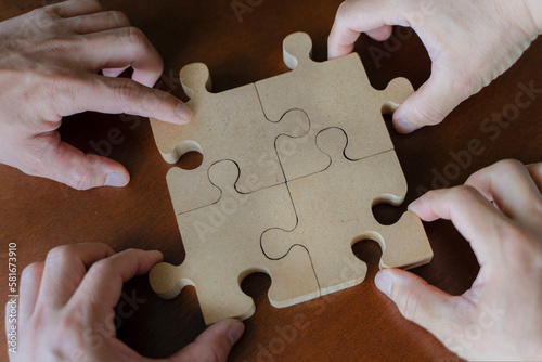 Business people team sitting around meeting table and assembling wooden jigsaw puzzle pieces unity cooperation ideas concept