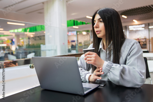 A young woman drinks coffee while working at a laptop