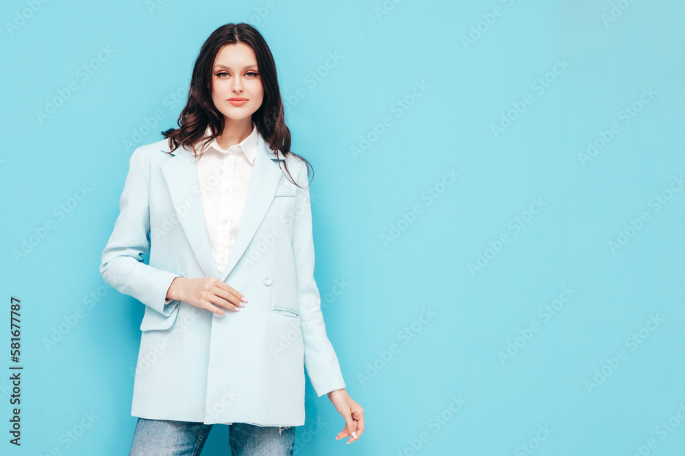 Portrait of young beautiful brunette woman wearing nice trendy blue suit jacket and jeans. Sexy fashion model posing in studio. Fashionable female isolated on blue. Cheerful and happy Portrait of young beautiful brunette woman wearing nice trendy blue suit jacket and jeans. Sexy fashion model posing in studio. Fashionable female isolated on blue. Cheerful and happy
