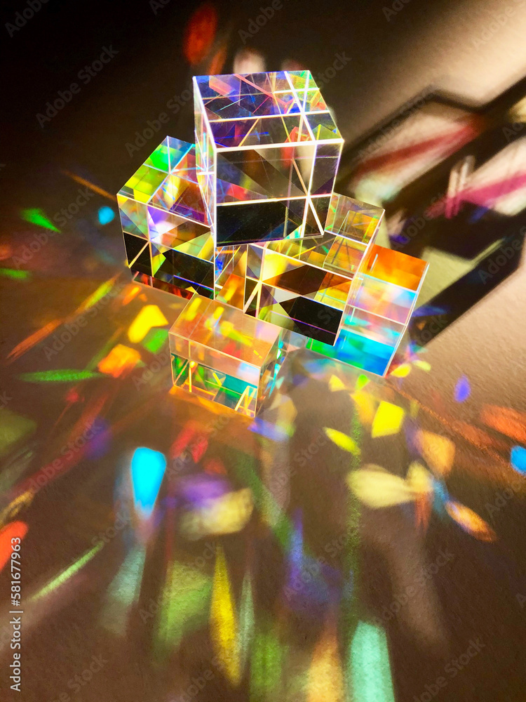 Cubic coloured dichroic glass disperse narrow beam of artificial light into colourful spectrum on texture white paper background. Colour combination with shade and shadow and reflection of light 