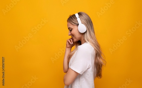 half-turned girl in white headphones on a yellow background with empty space