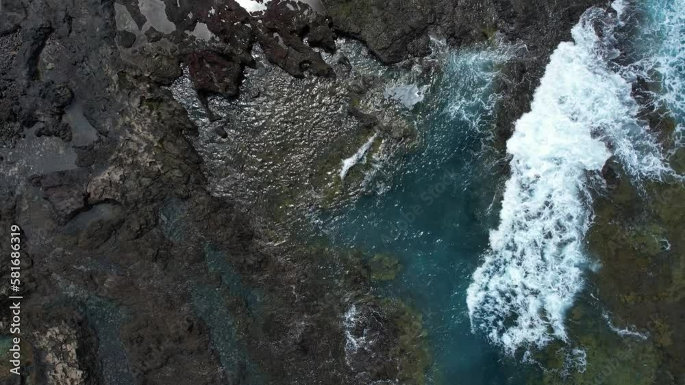 Top Down View Over A Volcanic Rocky Shoreline With Foaming Waves Splashing, Sky Reflecting In Small Puddles Top Down View Over A Volcanic Rocky Shoreline With Foaming Waves Splashing, Sky Reflecting In Small Puddles