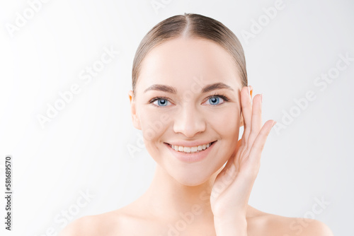 Portrait smiling beautiful young girl with perfect glowing skin and bare shoulders on light studio background. Holding hand showing Beautiful natural woman looking at camera Spa skincare and wellness.