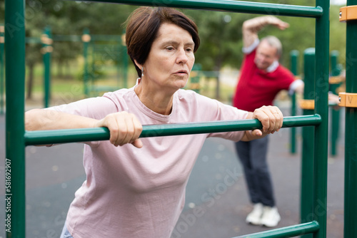 Mature woman doing push-ups from the crossbar on outdoor sports ground