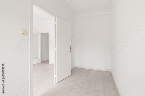 Spacious empty room with light walls and wooden laminate flooring with doors and access to another room. Concept apartment after renovation or hotel rooms. Copyspace