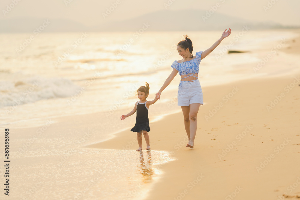 happy time of mom and daughter in dress black walking and run play on the beach with blur background beautiful sunset light in the sea