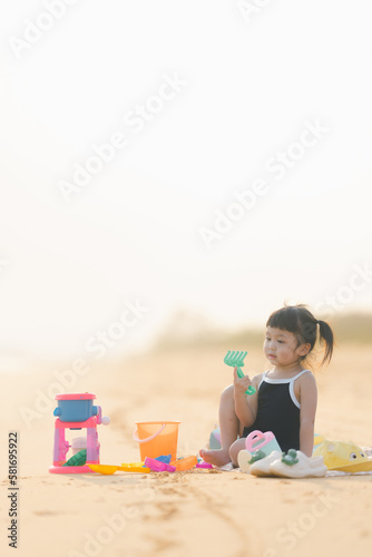 happy time of cute girl in dress black sit play sand scoop toy set on the beach with blur background beautiful sunset in the sea