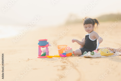 happy time of cute girl in dress black sit play sand scoop toy set on the beach with blur background beautiful sunset in the sea