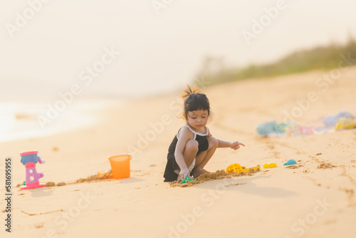 happy time of cute girl in dress black sit play sand scoop toy set on the beach with blur background beautiful sunset in the sea