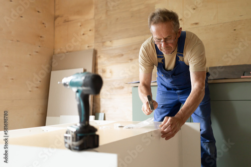 mature adult elderly senior man building wooden house, assembling furniture according to the instruction using different tool, drill, screwdriver. active old age, male hobby retirement