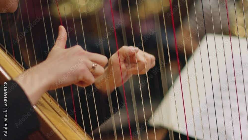 A slow motion video of a musican playing the harp in the middle register during a classical symphony orchestra rehearsal