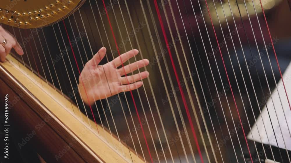 A slow motion video of a musician playing a glissando on a harp during a classical symphony orchestra concert