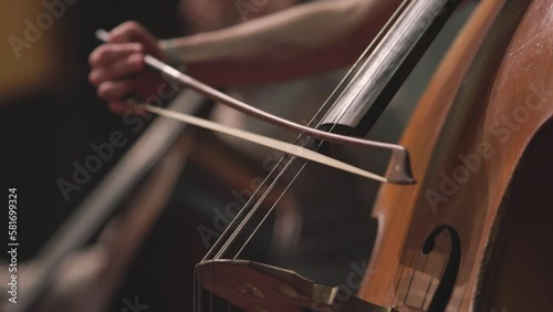 A double bass player in slow motion playing an acoustic double bass with a bow during a classical symphony orchestra rehearsal