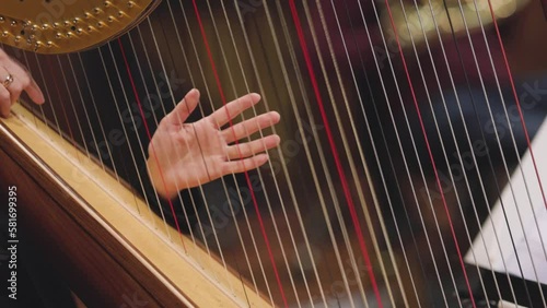 A slow motion video of a musician playing a glissando on a harp during a classical symphony orchestra concert