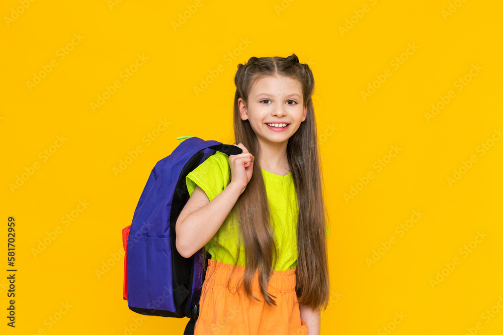 A schoolgirl with a backpack. A little girl with a satchel on her back. Teaching children. Supplementary education of the child. Educational, preparatory courses for school. Yellow isolated background A schoolgirl with a backpack. A little girl with a satchel on her back. Teaching children. Supplementary education of the child. Educational, preparatory courses for school. Yellow isolated background