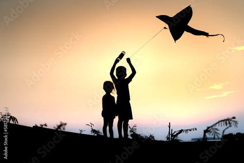 Silhouette of rural children flying kites at sunset.