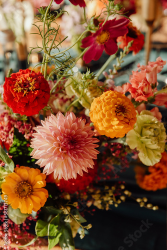 Detail of a table setting in a restaurant. Fresh flowers in red, white and orange with green twigs on a dark green tablecloth © Ilya.K