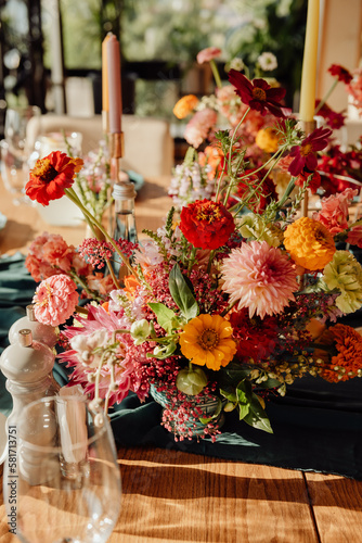 Detail of a table setting in a restaurant. Fresh flowers in red, white and orange with green twigs on a dark green tablecloth