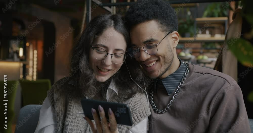 Slow motion of happy couple watching funny video on smartphone screen and laughing indoors in cafe. Relationship and gadgets concept. Slow motion of happy couple watching funny video on smartphone screen and laughing indoors in cafe. Relationship and gadgets concept.