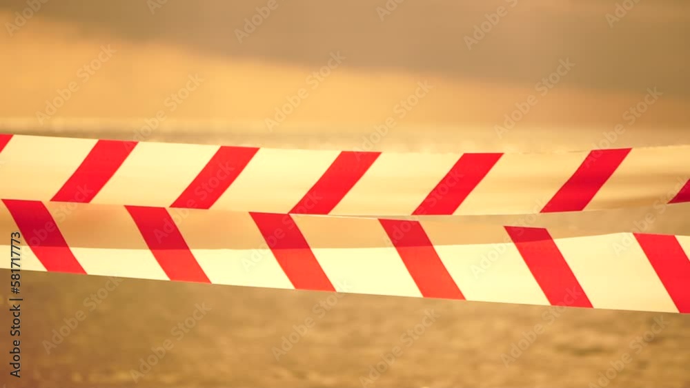Red white warning tape barrier ribbon swinging in the wind across exotic sea beach background without people. No entry Red White caution tape. No holiday concept, delayed travel, no summer plans Red white warning tape barrier ribbon swinging in the wind across exotic sea beach background without people. No entry Red White caution tape. No holiday concept, delayed travel, no summer plans