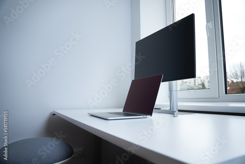 Stylish workplace  with modern gadgets. Emty Workspace for IT specialist. Remote job. Laptop and big screen on a desk. Close-up of closed laptop on white table against the window. 