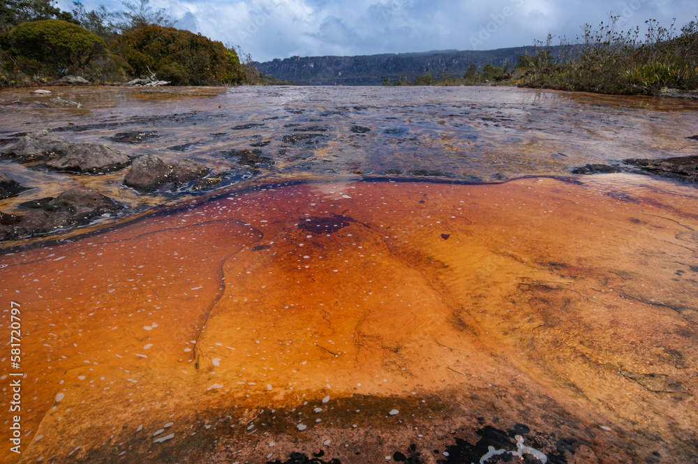 Orange and black rock structures in shallow river on the plateau of