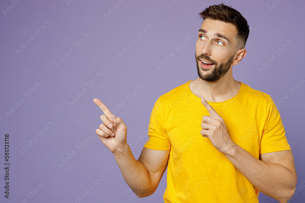 Young smiling happy man wear yellow t-shirt point index finger aside indicate on workspace area copy space mock up isolated on plain pastel light purple background studio portrait. Lifestyle concept. Young smiling happy man wear yellow t-shirt point index finger aside indicate on workspace area copy space mock up isolated on plain pastel light purple background studio portrait. Lifestyle concept.