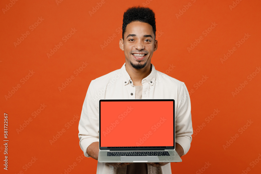 Young happy student IT man of African American ethnicity wear light shirt casual clothes hold use work on laptop pc computer with blank screen workspace area isolated on orange red background studio. Young happy student IT man of African American ethnicity wear light shirt casual clothes hold use work on laptop pc computer with blank screen workspace area isolated on orange red background studio.