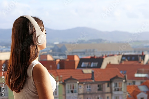 Teen girl with headphones listening to music or podcast from a balcony © TopMicrobialStock
