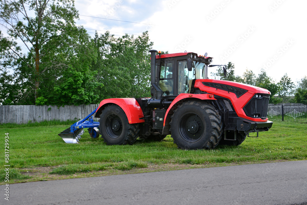 A red tractor with black wheels is parked on a grass on the field isolated, close-up A red tractor with black wheels is parked on a grass on the field isolated, close-up