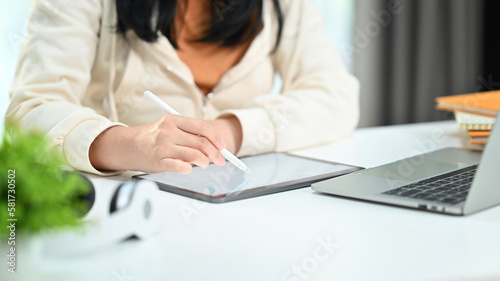 Cropped view of female employee searching online information on digital tablet, sitting at her workplace