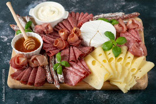 Cheese, prosciutto, salami on a wooden square board on a black stone background.