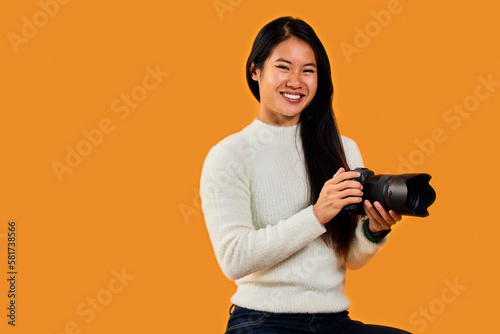 Close-up portrait of a smiling Asian female photographer, holding a camera.