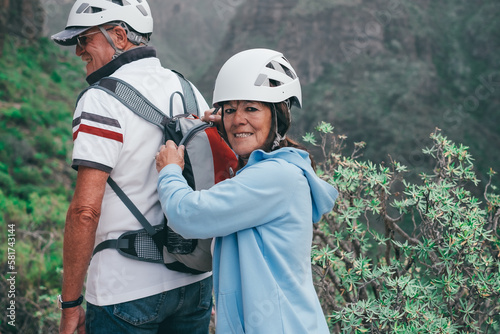 Rear view of two senior hikers with backpack and helmets enjoying trekking day on mountain - Active climbing tourists enjoying holidays and healthy lifestyle - Freedom, success sport concept