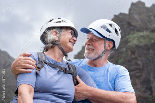 Portrait of Senior couple of hikers with helmets and backpacks resting on the top of mountain - Smiling climbing tourists enjoying holidays and healthy lifestyle in trekking day