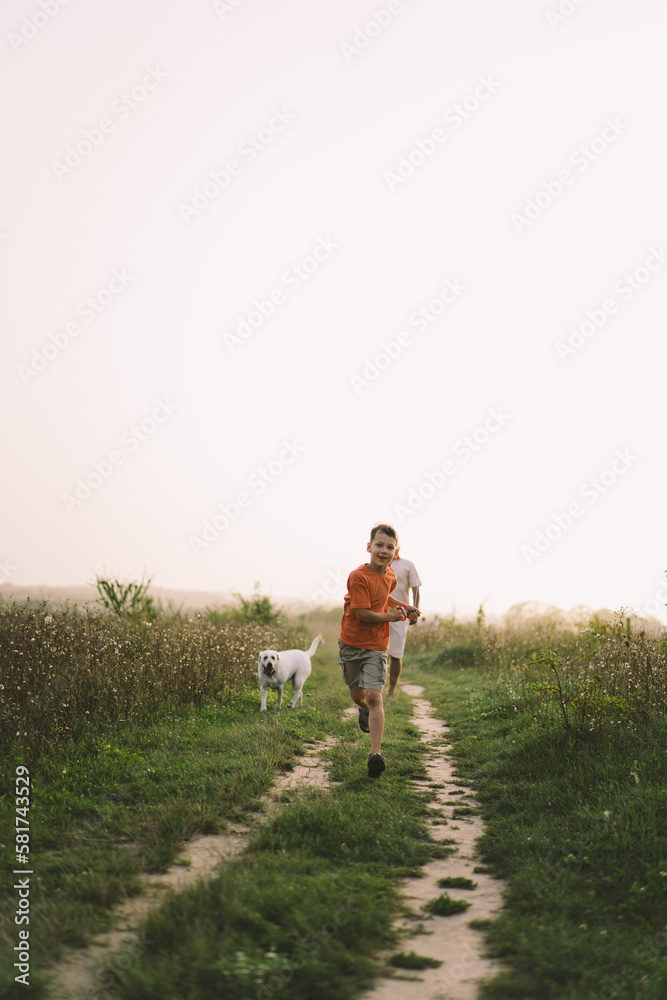 Portrait of a funny boy in a orange T-shirt and playing outdoors on the field at sunset. Happy child, lifestyle.
