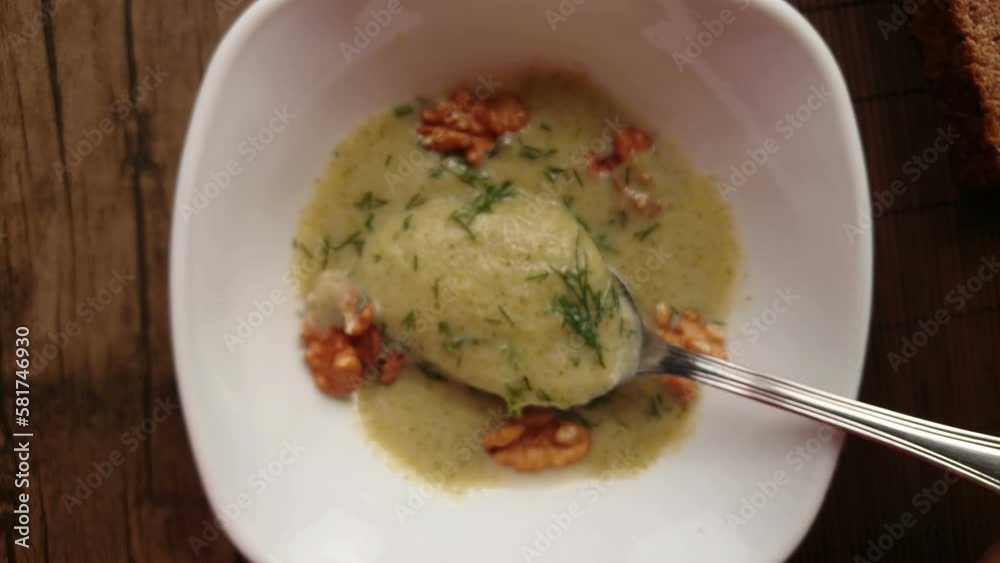 Spoon scooping broccoli soup with dill pieces from plate Spoon scooping broccoli soup with dill pieces from plate