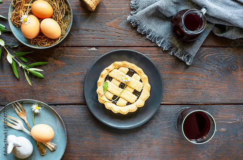 Easter food concept in farm rustic style. Egg, olive tree branch, crostata pie, red wine, decor on wood background. Top view