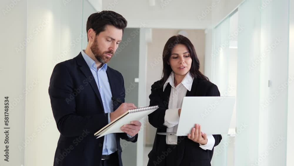 Charming woman holds a laptop and talks to her colleague at work. The man actively listens to his manager and takes notes on important information in his notebook. Communication, time management. Charming woman holds a laptop and talks to her colleague at work. The man actively listens to his manager and takes notes on important information in his notebook. Communication, time management.